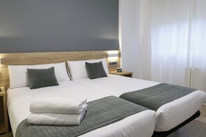 A double bed with white and gray bedding, a wooden headboard, and a nightstand with a Wi-Fi symbol. - Alda Narón (Naron)