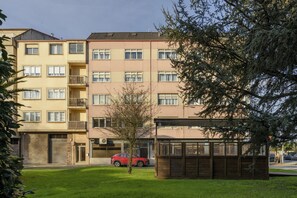 A multi-story residential building with balconies, a small tree, and a red car parked in front.