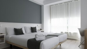 Et moderne hotelværelse med to senge, et natbord og udsigt til det fri gennem lette gardiner.