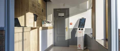 Un espace d’accueil comprenant un comptoir en bois, une porte et un kiosque en libre-service.