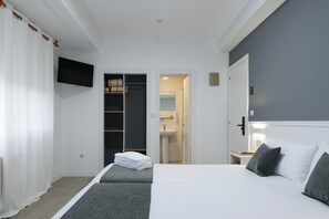 Habitación de hotel con cama, televisor, armario y baño visible a través de una puerta abierta.