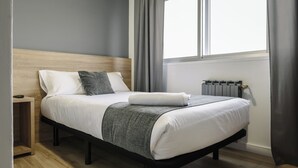 Et moderne soveværelse med sengegavl i træ, en pænt redt seng med hvide sengetøj og et gråt tæppe, et natbord og en radiator.
