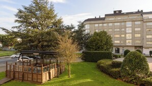 Ein Gebäude mit einem großen Baum davor, einer Holzkonstruktion mit Bänken und einem gepflegten Rasen.