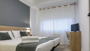Et moderne hotelværelse med en stor seng, et fjernsyn på et træstel og et skrivebord med en stol.