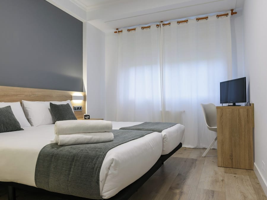 Una habitación de hotel moderna con una cama grande, un televisor sobre un soporte de madera y un escritorio con una silla.