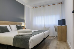 Una habitación de hotel moderna con una cama grande, un televisor sobre un soporte de madera y un escritorio con una silla.