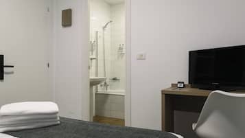 Une chambre d’hôtel comprenant un lit, un bureau avec une télévision, une salle de bain avec douche et lavabo, ainsi qu’une pile de serviettes.