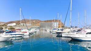 A marina with multiple boats docked, a large building in the background, and a clear blue sky. - Villagrancanaria (Mogan)