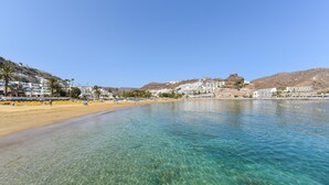 A beach with clear water, sandy shore, and buildings in the background. - Villagrancanaria (Mogan)