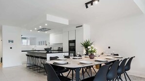 A modern kitchen with a central island, a dining area with a round table and black chairs, and a large potted plant. - Modern & Spacious with Wellness (Kortrijk)