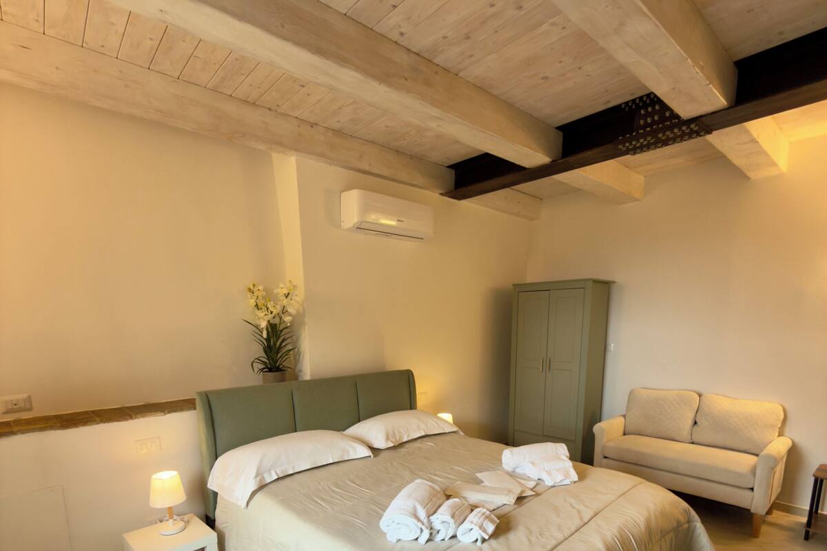 Un dormitorio con cama, mesita de noche, lámpara, aire acondicionado, armario verde y un sofá.