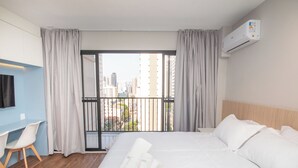 A hotel room with a bed, a desk, and a view of the cityscape through a balcony. - Perdizes Smart Experience - Allianz (São Paulo)