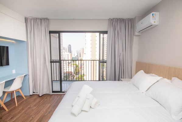 A hotel room with a bed, a desk, and a view of the cityscape through a balcony. - Perdizes Smart Experience - Allianz (São Paulo)