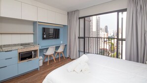 A modern hotel room with a bed, a small kitchenette, a seating area with chairs, and a large window with a city view. - Perdizes Smart Experience - Allianz (São Paulo)