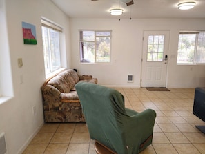Una sala de estar con un sofá estampado, un sillón verde y una puerta con ventana.