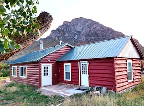 A red log cabin with a metal roof, white doors, and windows, set against a mountainous backdrop. - Cabin get-away in the Unaweep Canyon (Whitewater)