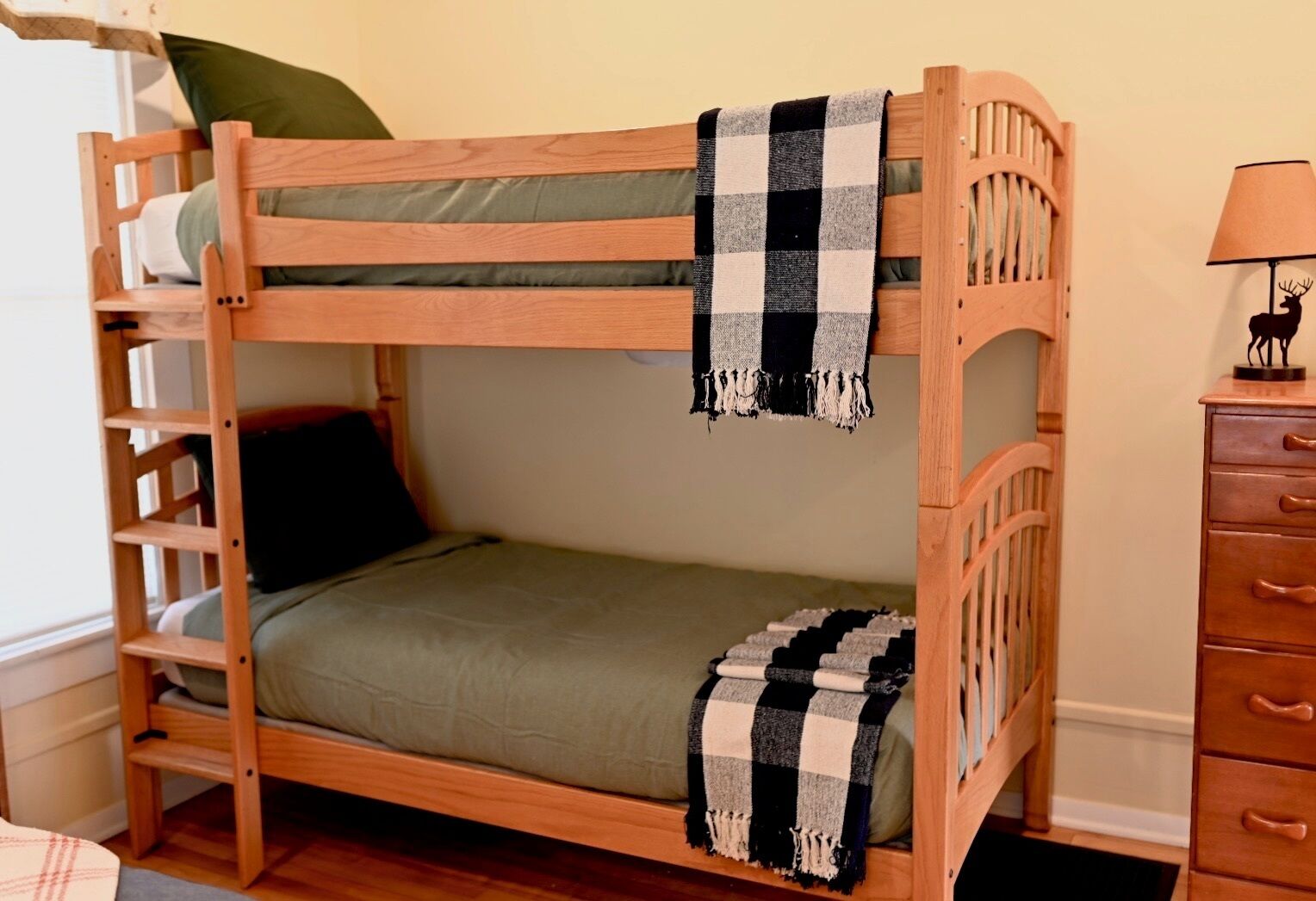 Una cama litera de madera con escalera, colchón verde y manta a cuadros.