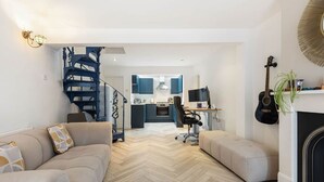 Una sala de estar moderna con piso de espiga, una escalera, una cocina al fondo y una chimenea.