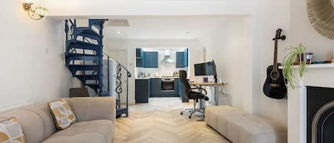 Ein modernes Wohnzimmer mit Fischgrätparkett, einer Treppe, einer Küche im Hintergrund und einem Kamin.