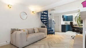 Una sala moderna con un sofá, suelo de espiga, una escalera y una zona de cocina.
