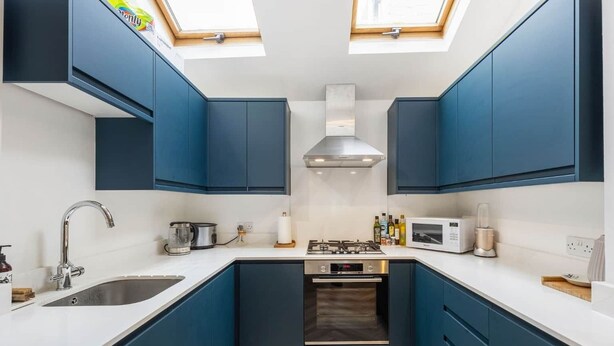 Una cocina compacta con armarios azules, un lavamanos de acero inoxidable, una estufa a gas y un microondas.