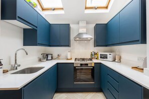 A compact kitchen with blue cabinets, a stainless steel sink, a gas stove, and a microwave.