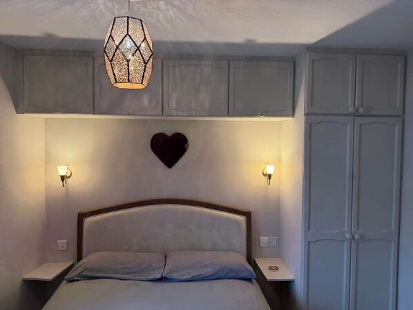 A bedroom with a bed, bedside lamps, a heart-shaped decoration, and a wardrobe.