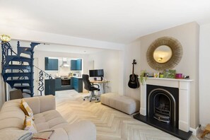 A modern living room with a sofa, a fireplace, and a kitchen in the background.