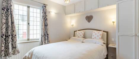 A bedroom with a bed, curtains, a wall-mounted light, and a radiator.