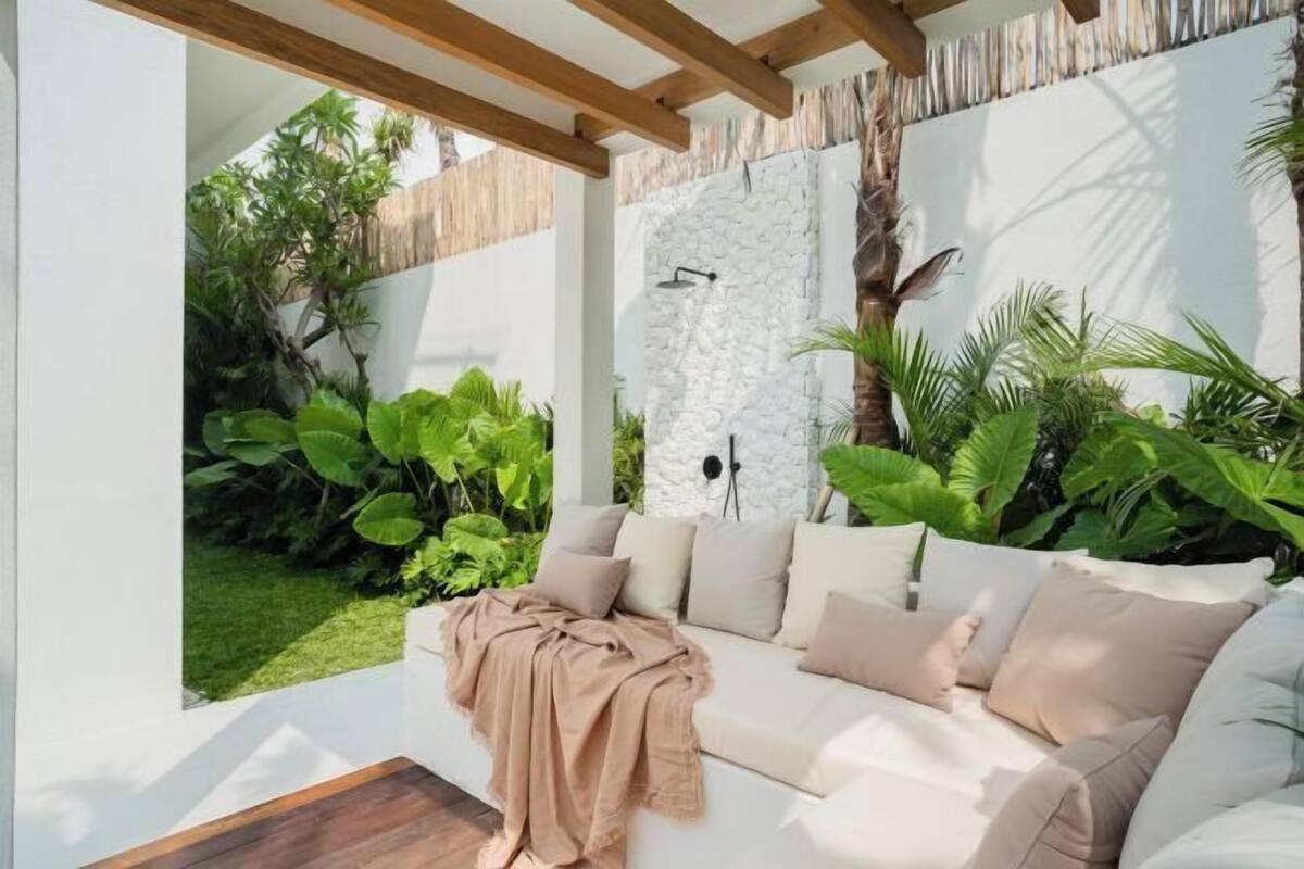 A modern outdoor living area with a white sofa, a stone wall, and lush greenery.