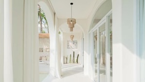 A bright hallway with a modern chandelier, glass doors, and a view into a room with a bed and a plant. - Mazari Villas (Bali)
