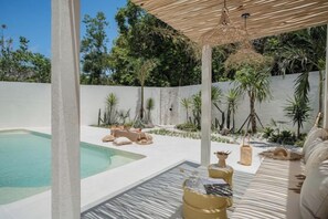 A pool area with a pergola, lounge chairs, and a small garden with palm trees. - Mazari Villas (Bali)