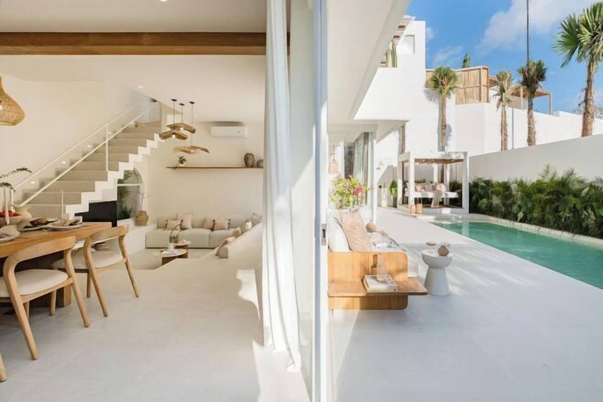 A modern interior with a staircase, a dining area, a living room, and a poolside seating area.
