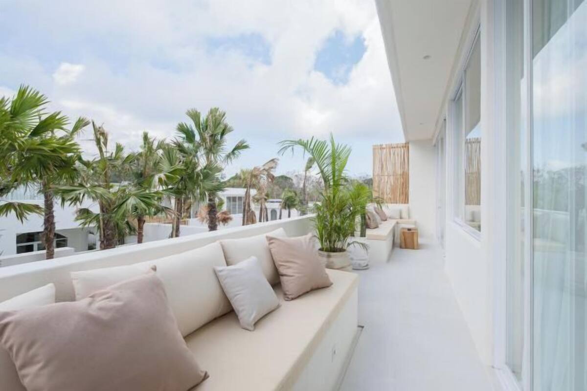 A balcony with a sofa, cushions, and potted plants.