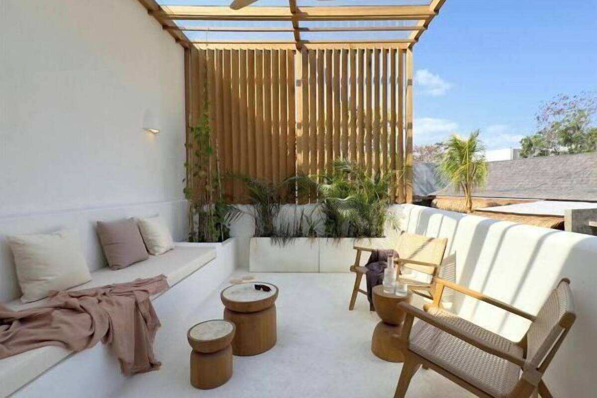 A modern outdoor seating area with a white sofa, wooden side tables, and a wooden chair.