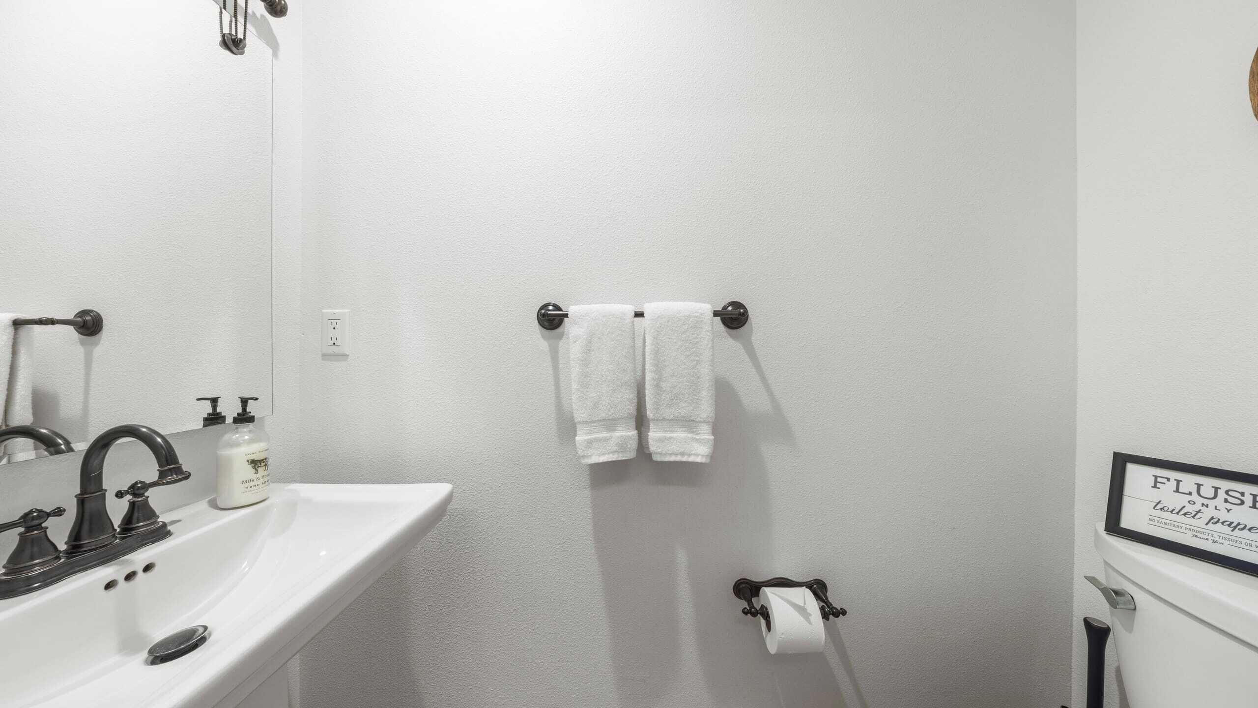 A bathroom with a white sink, two faucets, a mirror, a towel rack with two towels, a toilet paper holder, and a sign indicating the toilet is for flushing only.