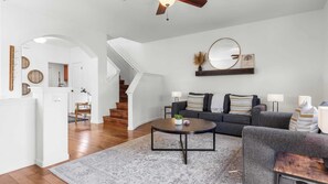 Una sala de estar moderna con un sofá gris, una mesa de centro redonda y una escalera que lleva a otro nivel.