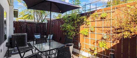 A patio with a table and chairs, a large umbrella, and a wooden fence with climbing plants.