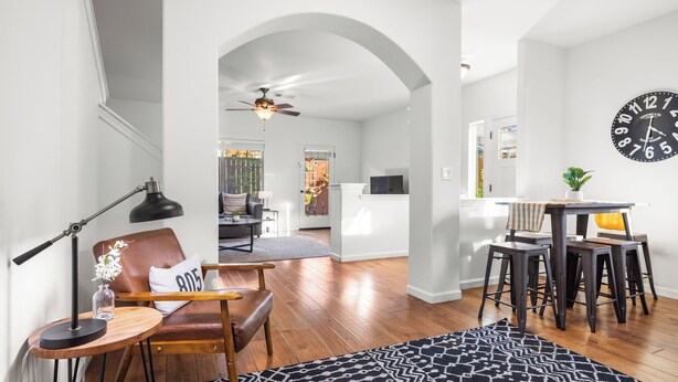 A spacious living area with a wooden floor, a leather chair, a dining table with stools, a ceiling fan, and a clock on the wall. - Walk to Downtown Paso & Sip Local Wine Under the Stars Casa Robles by Avantstay (Paso Robles)