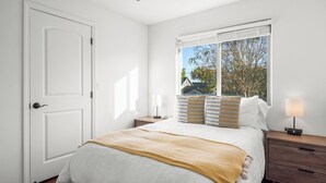A bedroom with a bed, a window with blinds, a bedside table with a lamp, and a door. - Walk to Downtown Paso & Sip Local Wine Under the Stars Casa Robles by Avantstay (Paso Robles)