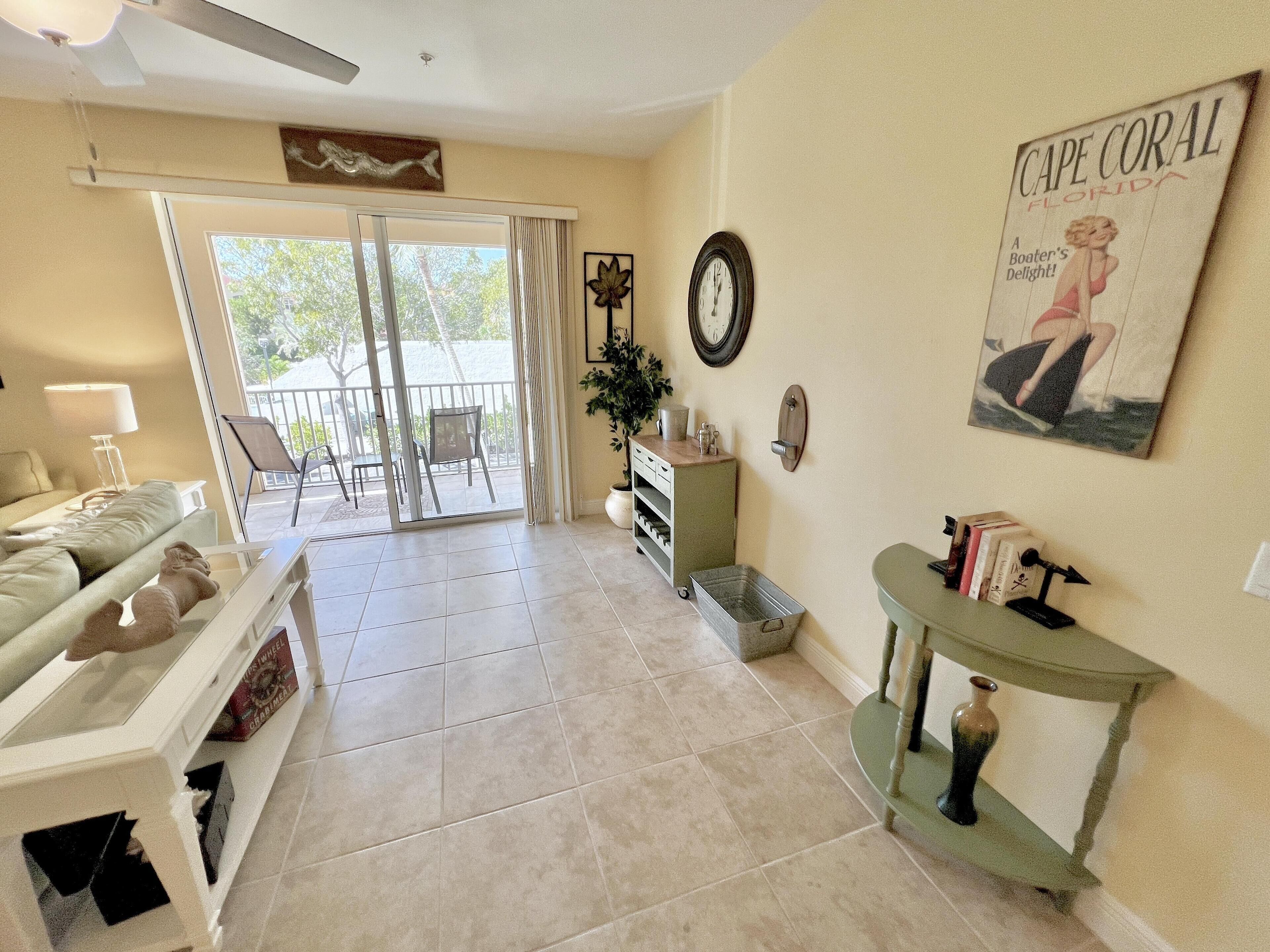 A spacious living room with a sliding glass door leading to a balcony, a sofa, a coffee table, and a small side table with books and a vase.