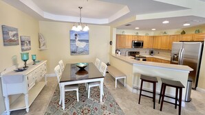 A modern kitchen with wooden cabinets, a stainless steel refrigerator, and a dining area with a white table and chairs. - TOP FLORIDA's Villa Porto Vista (Cape Coral)