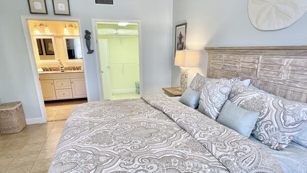 A bedroom with a large bed, a nightstand with a lamp, a dresser, and a closet with a mirror. - TOP FLORIDA's Villa Porto Vista (Cape Coral)