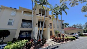 A multi-story residential building with a beige facade, balconies, and a parking area with a white car. - TOP FLORIDA's Villa Porto Vista (Cape Coral)