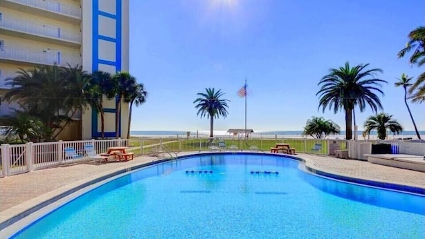 A swimming pool with a clear view of the ocean, surrounded by palm trees and a white fence. - Tranquil villa with private beach, 2br/2ba 3 pools, complex on beach!! Patio (Sarasota)