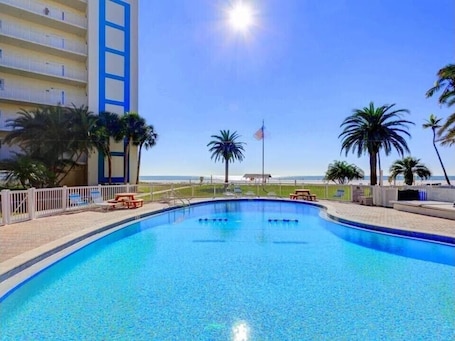 A swimming pool with a clear view of the ocean, surrounded by palm trees and a white fence.