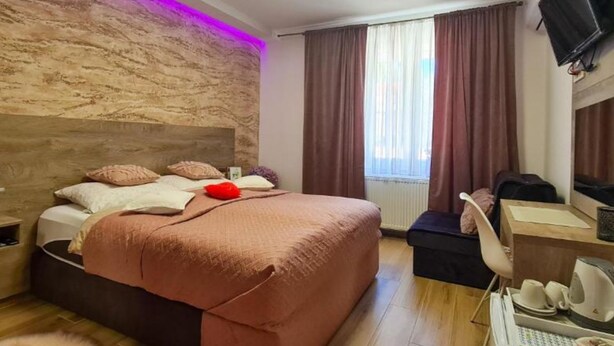 Moderni hotellihuone, jossa on suuri sänky, työpöytä tuolilla, seinälle asennettu taulutelevisio ja ikkuna, jossa on verhot.