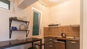 Cozinha compacta com bancada escura, janela com persianas, pia e lava-louças embutida.