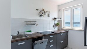 Une cuisine moderne avec des meubles gris, un plan de travail en bois, un lave-vaisselle encastré et une fenêtre donnant sur la mer.