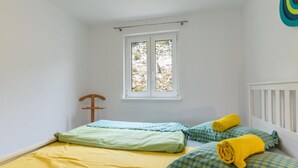 Une petite pièce lumineuse, avec un lit simple, une fenêtre et une chaise en bois.